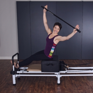 Woman seated on box and arm upright while holding the pole.