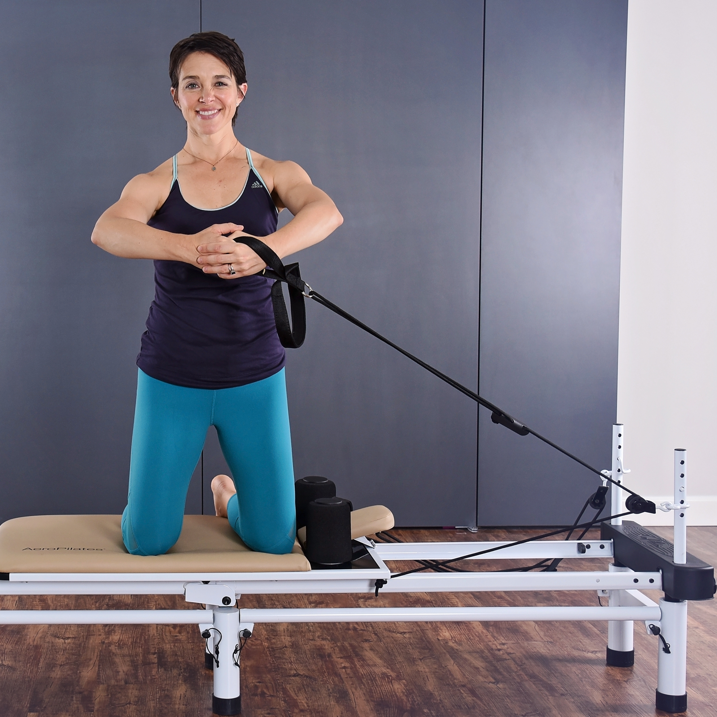 Woman kneeling on Padded Platform while pulling the Hand and Footstraps.