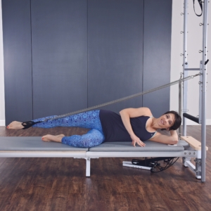 Woman lying down on pilates and stretch her leg with footstrap.