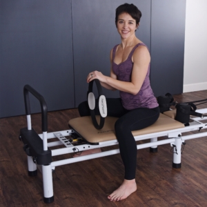 Seated woman in the center on the pilates and holding a magic circle.