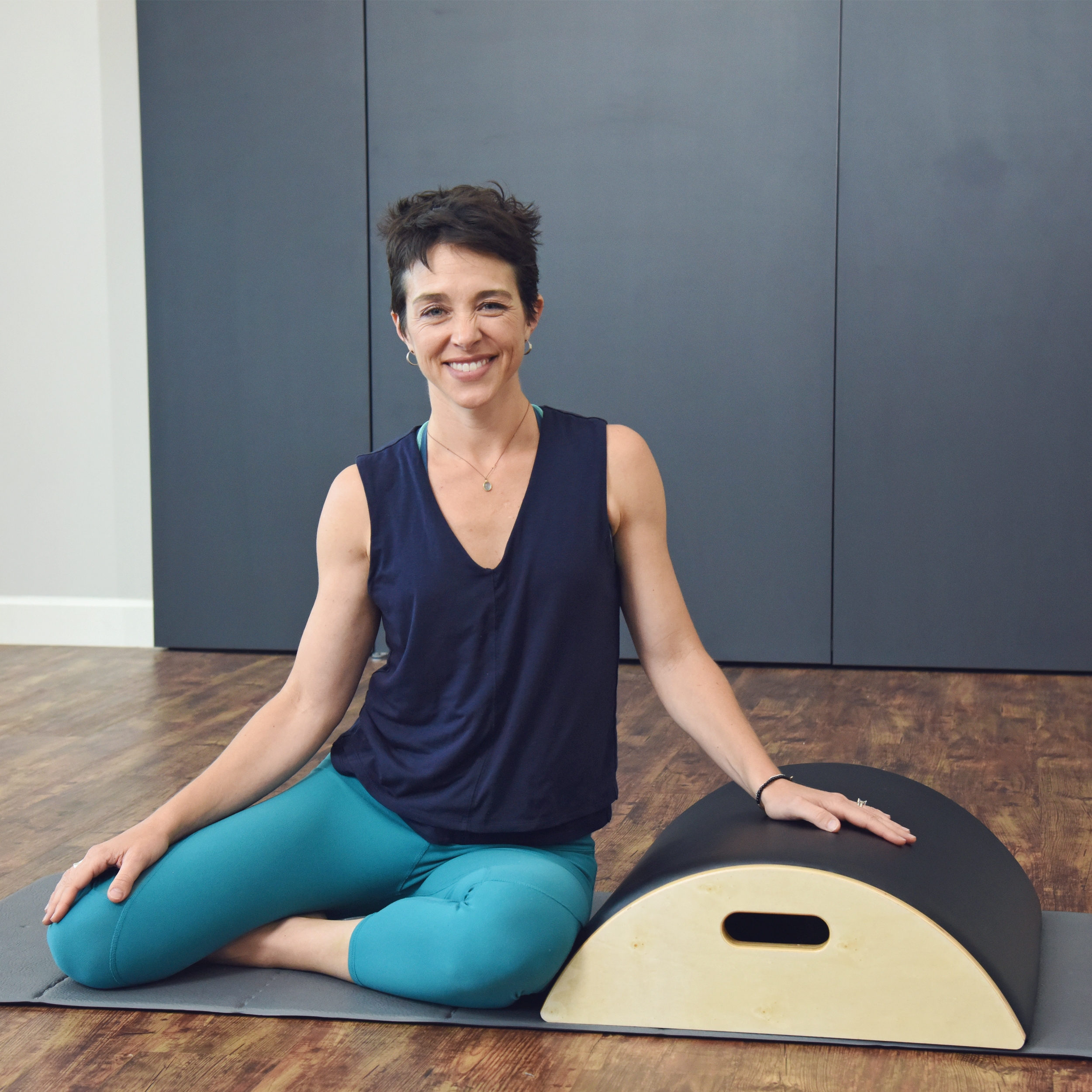 Woman smiling and seated aside on Aeropilates Arc Barrel.