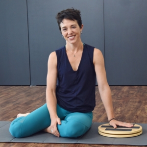 Woman holding and seated aside on Aeropilates Rotational Disc.